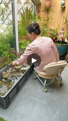 a woman sitting in a chair next to a window filled with lots of plants and rocks