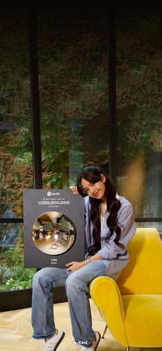 a woman sitting on a yellow chair holding up a framed photo with an object in front of her