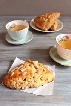 three tea cups and two scones on a table