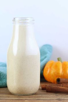 a glass bottle filled with cinnamon spice sitting on top of a wooden table next to an orange pumpkin