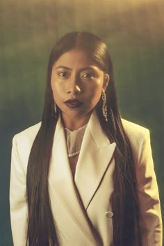 a woman with long black hair wearing a white suit and silver earrings is making a face