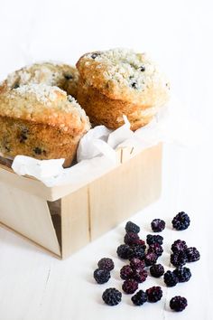 two muffins in a wooden box with some berries on the table next to it