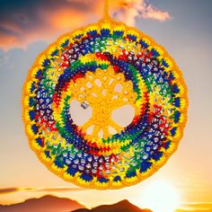 a crocheted sun catcher hanging in the air with mountains in the background at sunset