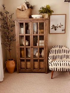 a living room with a chair, potted plant and an old china cabinet in the corner