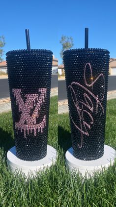 two plastic cups sitting in the grass with writing on them and straws sticking out of each cup