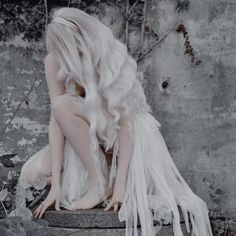 a woman with long white hair sitting on top of a stone pillar in front of a wall