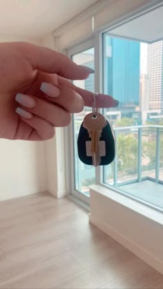 a woman's hand holding a house key in front of a window with the city outside