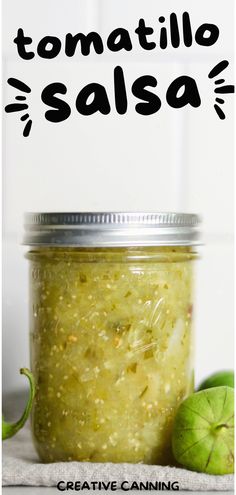 a jar filled with green salsa next to an apple