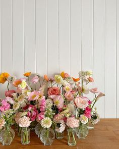 a group of vases filled with flowers on top of a wooden table in front of a white wall