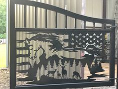 a metal gate with an american flag and horses in the woods on it's side