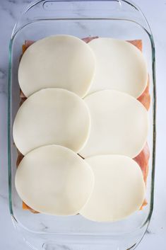 slices of ham and cheese in a glass dish on a marble counter top, ready to be cooked