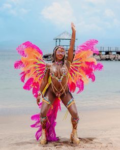 a woman dressed in pink and orange on the beach with her arms up, dancing