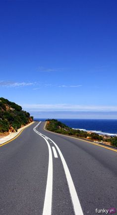 an empty road near the ocean on a sunny day with blue sky and water in the background