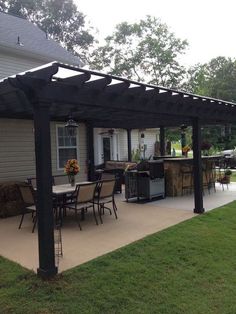 a patio covered in black plastic furniture next to a white house with an outdoor kitchen