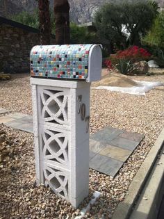 a white mailbox sitting in the middle of a gravel area next to a garden