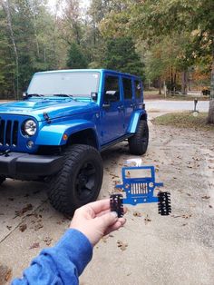 a blue jeep is parked in front of a man holding a remote control device with his hand