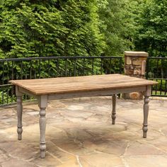 a wooden table sitting on top of a stone floor next to a fence and trees