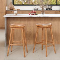 two stools sit in front of a kitchen island with an open window overlooking the trees