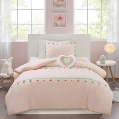 a bed with pink comforter and pillows on top of it next to a window