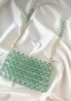 a green beaded purse sitting on top of a white cloth