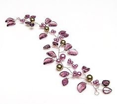 a necklace with purple beads and leaves on it's side, sitting on a white surface