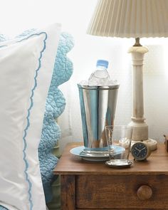 a wooden table topped with a metal shaker next to a night stand and lamp