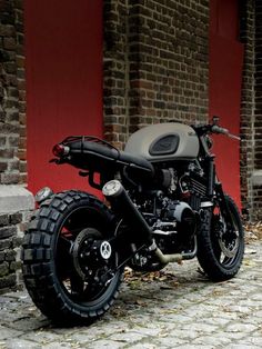 a black motorcycle parked on top of a cobblestone street next to a red building