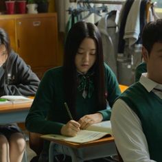 three students are sitting at desks writing