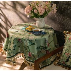 a table topped with a vase filled with flowers next to two pillows on top of a chair