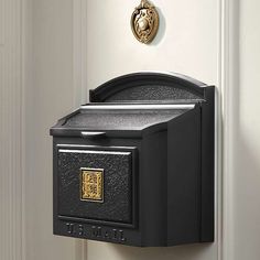 a black mailbox mounted to the side of a white door with a gold emblem on it