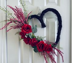 a heart shaped wreath with red roses and greenery on the front door to a house