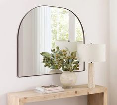 a mirror sitting on top of a wooden table next to a vase filled with flowers