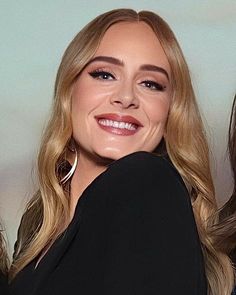 a woman with long blonde hair and large hoop earrings on her face, smiling at the camera