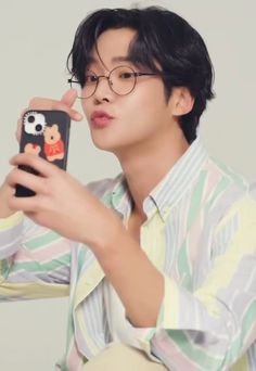 a young man is taking a selfie with his cell phone while wearing glasses and a striped shirt