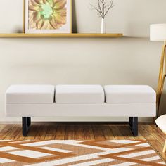 a white bench sitting on top of a hard wood floor next to a painting and lamp