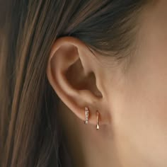 a woman's ear with two small diamond hoop earrings