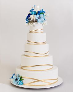 a white and gold wedding cake with blue flowers on top