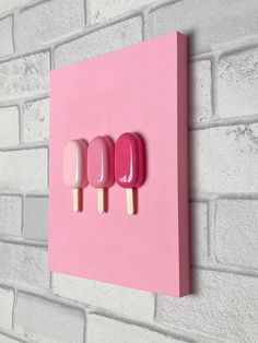 three popsicles mounted to a pink brick wall