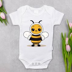 a white baby bodysuit with a cute cartoon bee on it's chest, sitting next to tulips