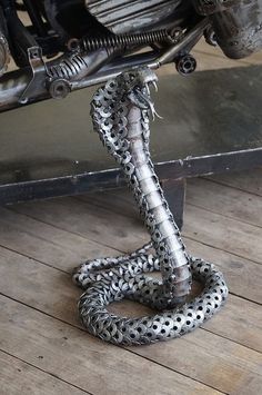 a metal snake sitting on top of a wooden floor next to a motor bike tire