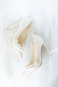 two pairs of white shoes with pearls on the toes and one pair of high heeled shoes