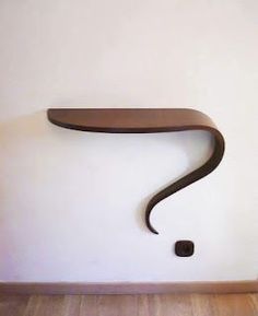 a wooden shelf with a question mark on the wall next to a wood floor in front of a white wall