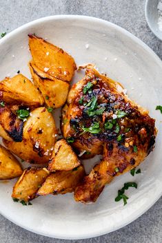 a white plate topped with chicken and potatoes covered in parmesan cheese, garnished with herbs