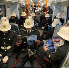 men in uniforms are sitting on a train and looking at their ipads while wearing white hats