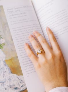 a woman's hand is holding an open book with a diamond ring on it