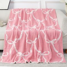 a pink blanket with white bows on it sitting in front of a couch next to a window