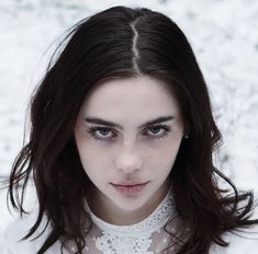 a woman with dark hair and blue eyes looks at the camera while standing in snow