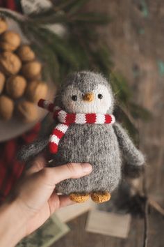 a hand holding a small stuffed penguin in front of some nuts and pine cones on a wooden table