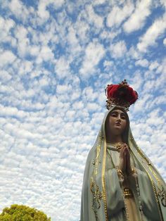 a statue of the virgin mary in front of a cloudy blue sky