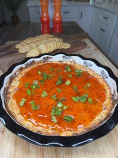 a pizza sitting on top of a wooden table next to crackers and an orange vase